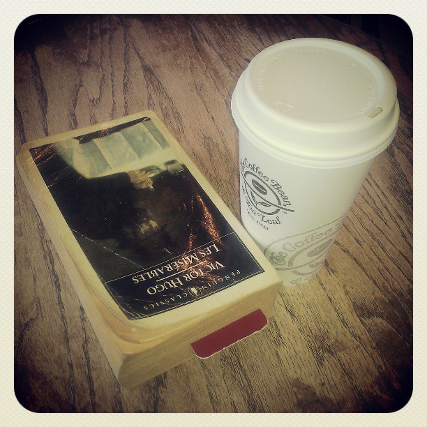 Picture of a book with a bookmark next to a cardboard coffee cup.
