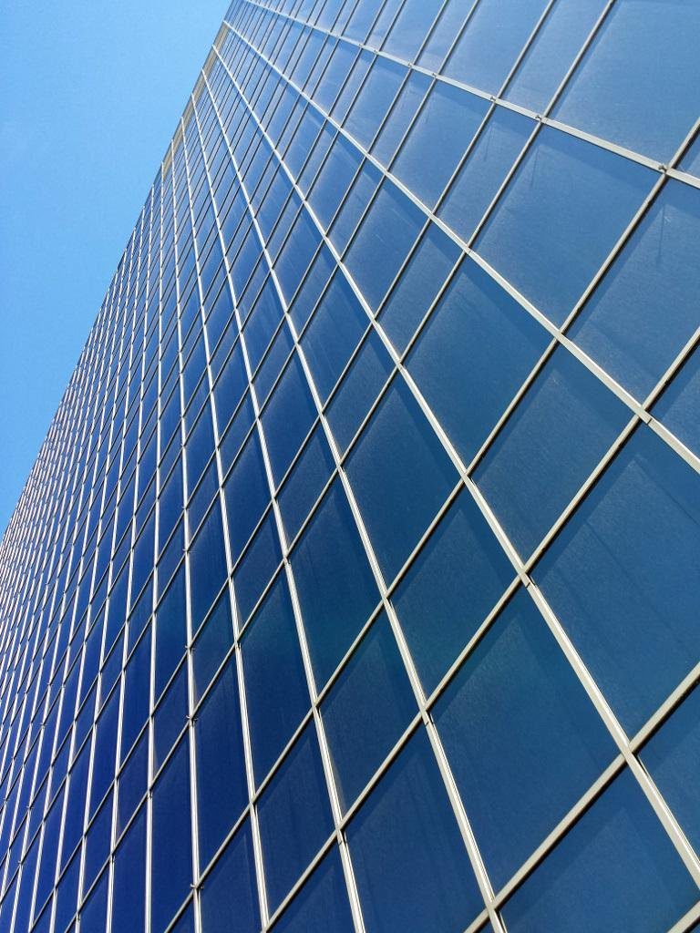 Looking up along the side of a building that's entirely covered with glass panes.