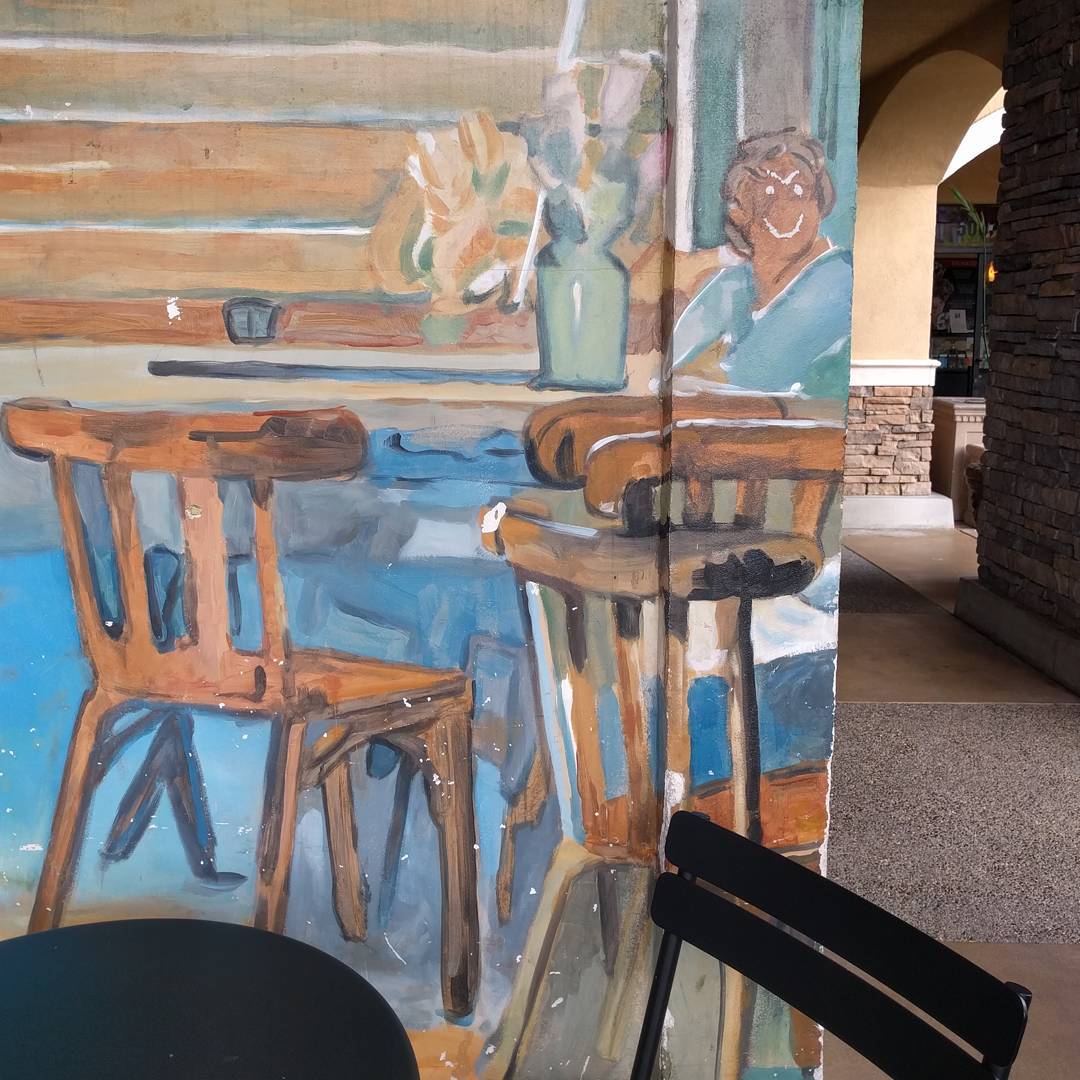 A mural of a coffee shop scene where someone has sketched an angry cartoon face onto one of the people.